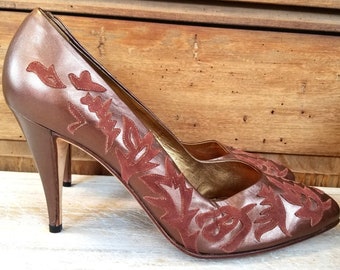 May include: A pair of brown leather high-heeled pumps with a floral design. The floral design is made of a contrasting brown suede material.