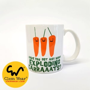 May include: White ceramic mug with a green and orange design. The mug features three cartoon carrots with smiling faces and the text "Have you got any more exploding carraats?"