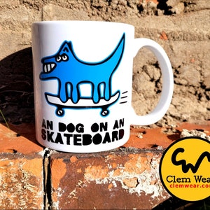 May include: White ceramic mug with a blue cartoon dog riding a skateboard. The mug has black text that reads "An Dog On An Skateboard".