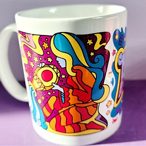 Peut inclure: Une tasse en céramique blanche avec un motif psychédélique coloré représentant une femme aux cheveux longs et flottants portant une robe à motifs rouge, orange, jaune et bleu. Le motif comprend également des étoiles et des volutes.