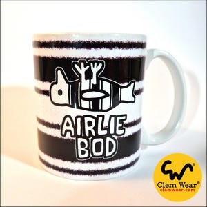 May include: White ceramic mug with black horizontal stripes and a white handle. The mug features a black and white graphic of a stylized creature and the words "AIRLIE BOD" in black. A yellow logo with black text is in the bottom right corner.