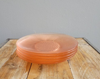 Puede incluir: Un conjunto de cuatro platos de vidrio rosa con un diseño acanalado. Los platos están apilados sobre una superficie de madera.