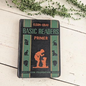 Op de afbeelding: Vintage "Elson-Gray Basic Readers Primer" boek. De zwarte kaft heeft groene en oranje accenten en toont illustraties van dieren en een kind met een hond. Het boek maakt deel uit van de Curriculum Foundation Series.