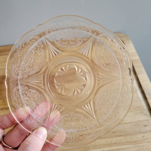 May include: A clear glass plate with a delicate etched floral pattern. The plate has a scalloped edge and a raised center.