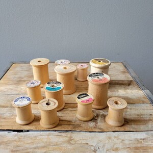 May include: A collection of wooden spools with various labels, including "Talon" and " Coats & Clark", on a wooden surface.