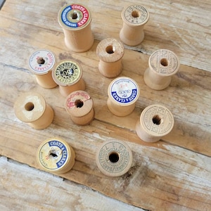 Pode incluir: Uma coleção de carretéis de linha de madeira vintage com vários rótulos, incluindo "Coats & Clark's" e "Corticelli".