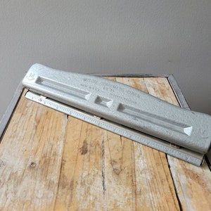 May include: A silver metal paper punch with the text "Mutual Stapler & Punch No. 24" and "Made in U.S.A. Pat. Pending" on the side. The punch is on a wooden surface.