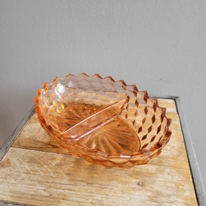 May include: A divided serving dish made of clear, peach-colored glass with a diamond pattern. The dish has a divided center section.