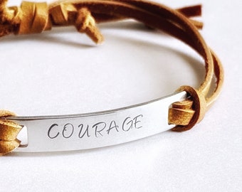 May include: A brown leather bracelet with a silver metal tag that says "COURAGE".