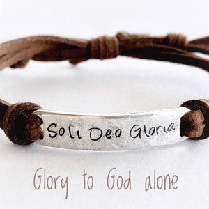 May include: Brown leather bracelet with a silver tag that reads "Soli Deo Gloria" and "Glory to God alone".