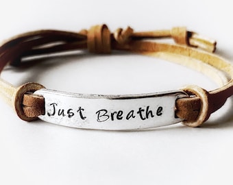 May include: A brown leather bracelet with a silver charm that says "Just Breathe".