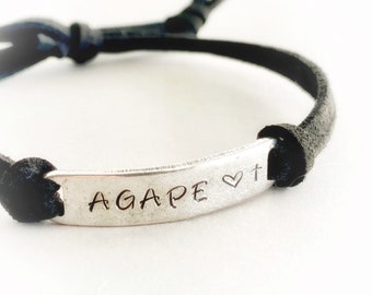 May include: Black leather bracelet with a silver charm that says "AGAPE" with a heart and cross symbol.