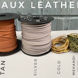 May include: Four spools of faux leather cord in tan, silver, gold, and olive green. The cords are wound around black spools and labeled with their colors.