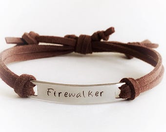 May include: A brown suede bracelet with a silver plate engraved with the word "Firewalker". The bracelet features a knotted design and is adjustable. A simple, yet stylish accessory.