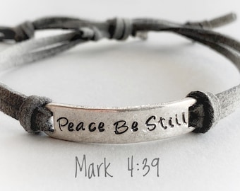 May include: Gray leather bracelet with a silver charm that reads "Peace Be Still Mark 4:39".