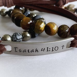 May include: Brown leather bracelet with a silver charm that reads "Isaiah 41:10 +" and brown, gold, and gray beads.