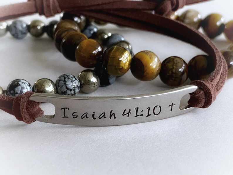 May include: Brown leather bracelet with a silver charm that reads "Isaiah 41:10 +" and brown, gold, and gray beads.