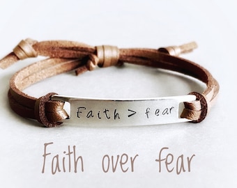 May include: A brown leather bracelet with a silver charm that reads "Faith > fear".