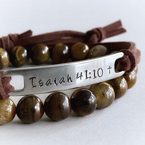 May include: Brown leather bracelet with a silver charm that reads "Isaiah 41:10 +" and tiger's eye beads.