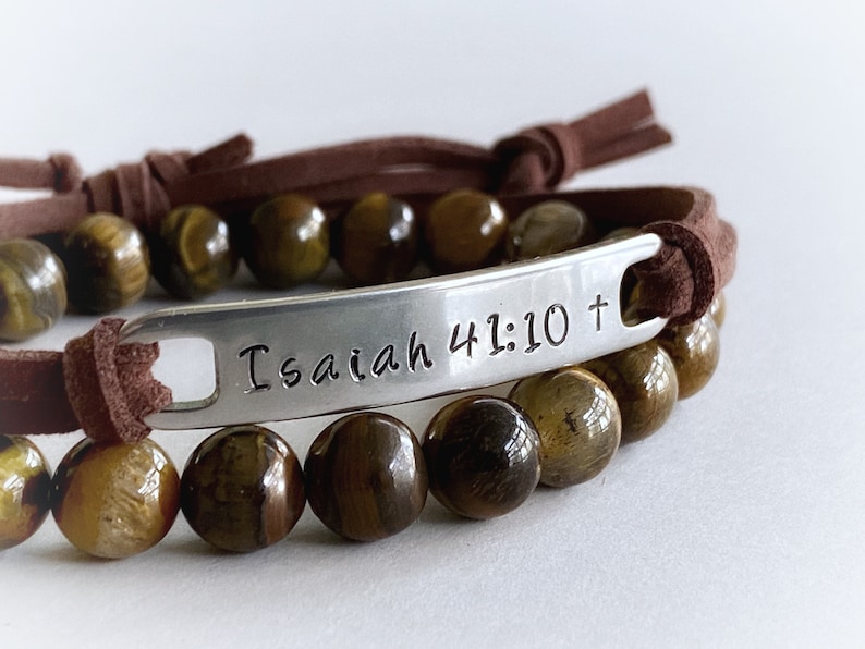 May include: Brown leather bracelet with a silver charm that reads "Isaiah 41:10 +" and tiger's eye beads.
