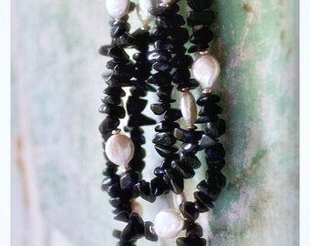May include: A multi-strand necklace featuring irregular black stone chips interspersed with smooth, white, oval-shaped pearls. The design consists of several strands of dark, textured stone beads accented by lustrous white pearls throughout the length.