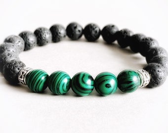 May include: A beaded bracelet featuring black lava rock beads and green malachite beads with black stripes. The bracelet also includes silver-colored metal accents. This piece of jewelry is a stylish accessory.