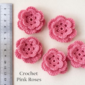 Könnte beinhalten: Fünf handgefertigte, rosa gehäkelte Rosen. Ein Metalllineal liegt neben den Blumen. Der Text "Crochet Pink Roses" ist sichtbar. Die Blumen haben einen Durchmesser von etwa 5 cm.