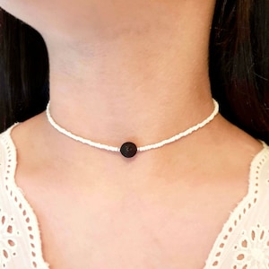 Puede incluir: Un collar gargantilla de cuentas blancas con una cuenta de lava negra en el centro.