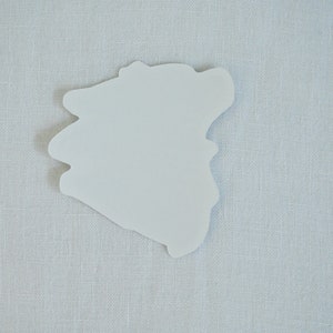 May include: A white paper sticker with an irregular, organic shape, resembling a cloud or a blob. The sticker is on a light gray textured background.