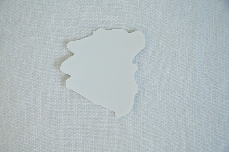 May include: A white paper sticker with an irregular, organic shape, resembling a cloud or a blob. The sticker is on a light gray textured background.