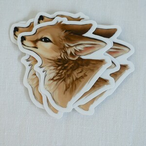May include: Three brown and white fox head stickers with white outlines. The fox is looking up and has a light brown nose and brown eyes.