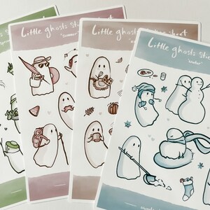 May include: Four sticker sheets featuring illustrations of ghosts in different seasons. The sheets are labeled "Little ghosts sticker sheet" with the season name below. The spring sheet features a green background with a ghost watering a plant. The summer sheet features a pink background with a ghost wearing a hat and sunglasses. The autumn sheet features a brown background with a ghost holding a cup of coffee. The winter sheet features a blue background with a ghost wearing a hat and scarf.