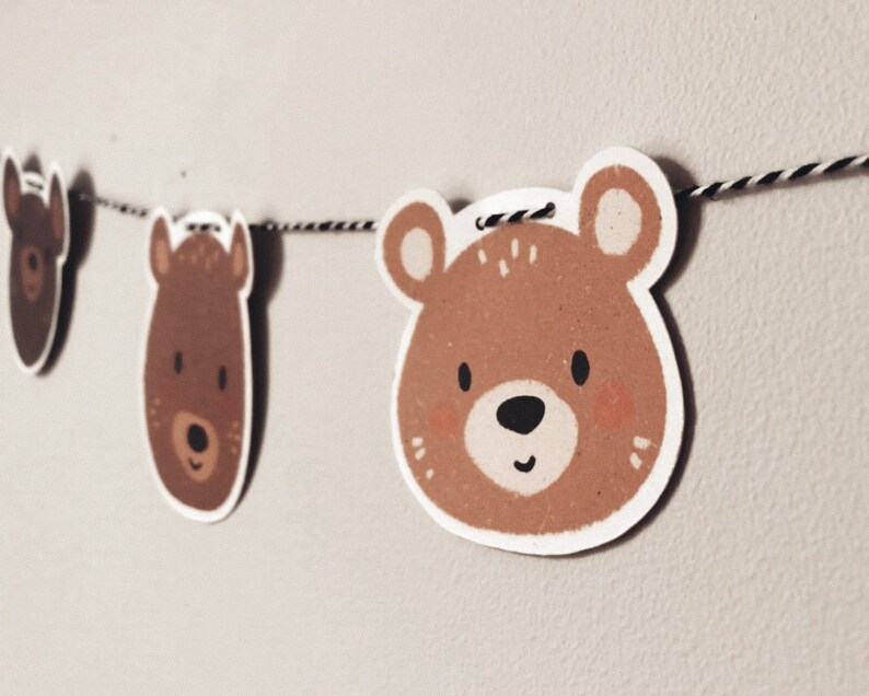 May include: A brown bear face garland with three bear faces on a white string. The bears have brown fur, black noses, and white eyes.