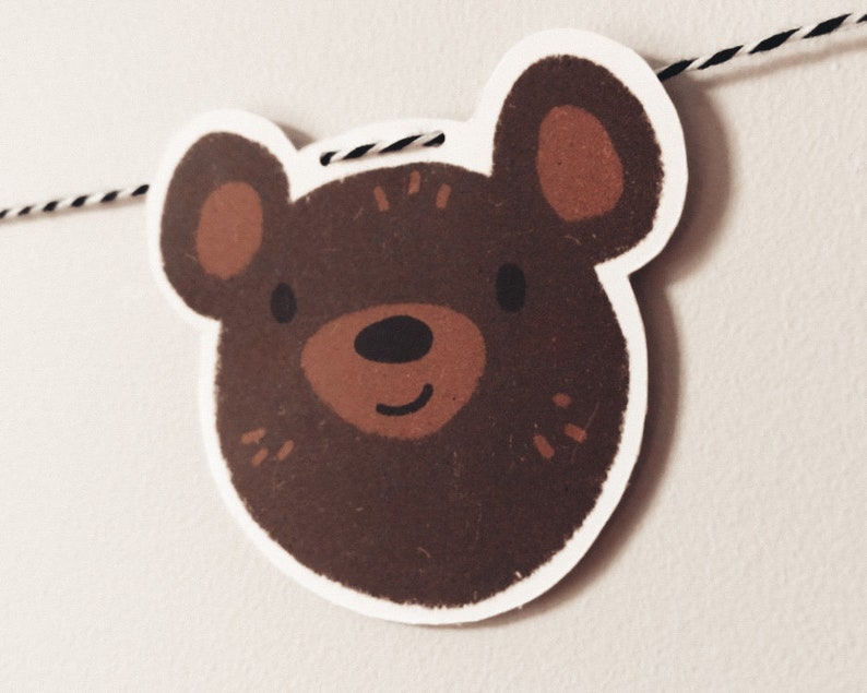 May include: A brown bear face with a white outline, brown ears, and a black nose. The bear is smiling and has a white background.