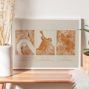May include: A framed print featuring three maps in gold foil. The maps are labelled with the text "Just one more drink", "Our first date", "1st March 2019 - 02", "OMG - YES!!", "Our engagement", "21st May 2022 - Fistral Beach", "We do", "Our wedding day", "8th June 2023 - Morden Hall".