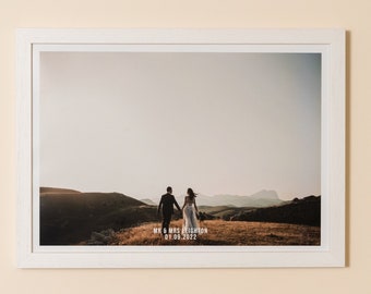 May include: A framed photograph of a wedding couple walking away from the camera on a grassy hilltop. The text "Mr & Mrs Leighton 01.08.2022" is printed below the couple.