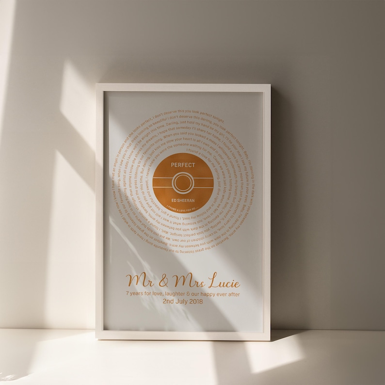 May include: A framed print featuring the song lyrics to "Perfect" by Ed Sheeran. The design includes a circular graphic with the song title and artist's name in a warm orange hue. The bottom of the print displays the names "Mr & Mrs Lucie" and a date.