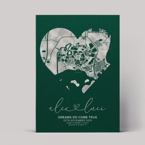 May include: A green background with a silver heart-shaped outline of a map. The text "alexluca" is written in cursive with a heart symbol between the names. The text "DREAMS DO COME TRUE" is written in all caps below the names. The date "25TH NOVEMBER 2023" is written below the text. The location "MAGIC KINGDOM, FLORIDA" is written below the date. The coordinates "28.4195 N, 81.5812 W" are written below the location.