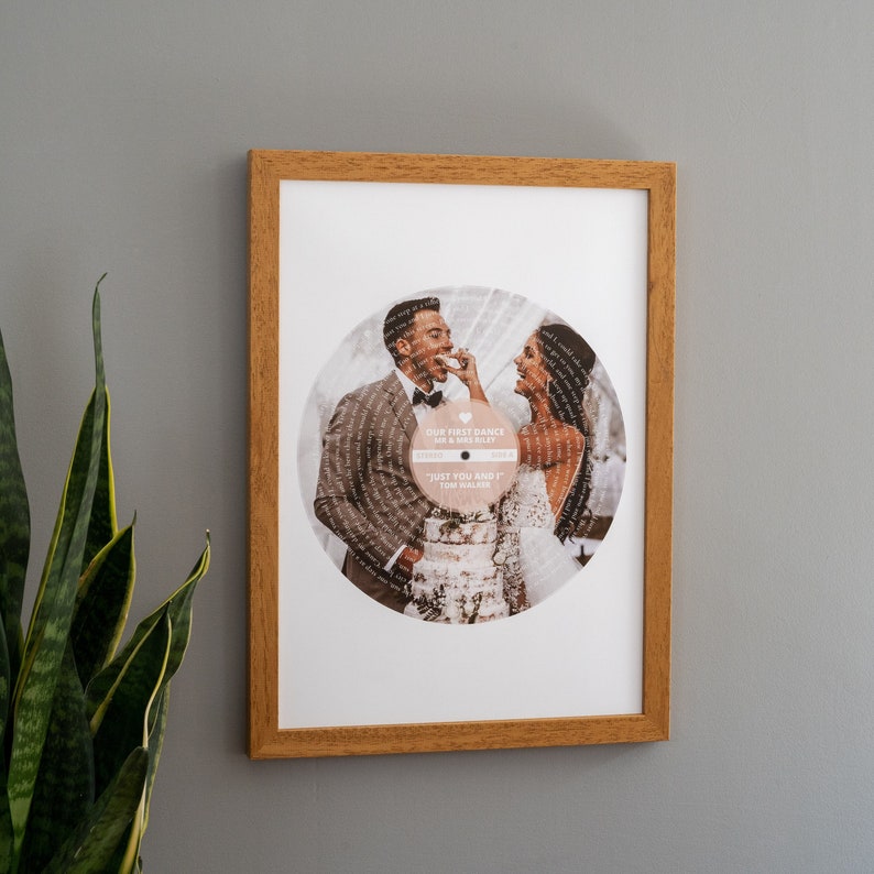 May include: A framed print of a wedding photo with the couple's first dance song lyrics printed around the edge. The lyrics are for the song "Just You and I" by Tom Walker. The couple is holding a piece of cake and smiling at each other.
