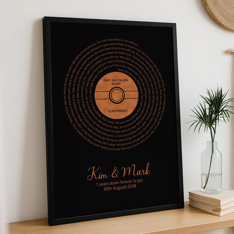 May include: Framed black print featuring a circular design resembling a vinyl record. The record's center displays "CANT HELP FALLING IN LOVE" and "ELVIS PRESLEY." Surrounding the record is song lyrics. Below, the print reads "Kim & Mark" and "7 years down forever to go! 10th August 2018."