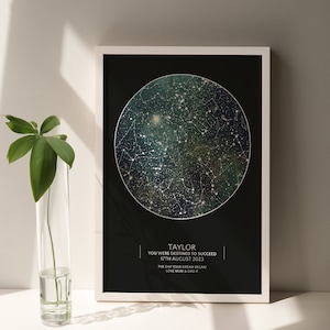 May include: A black and white framed print with a star map on a dark green background. The text "TAYLOR YOU WERE DESTINED TO SUCCEED 17TH AUGUST 2023 THE DAY YOUR DREAM BECAME LOVE MUM & DAD X" is printed below the star map.