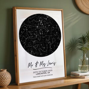 May include: A framed print displaying a black and white star map in a circular format. The print is inscribed with "Mr & Mrs Lewis", the date "20th October 2025", location "Lancaster, UK", and the words "THE START OF OUR FOREVER". The print is set in a wooden frame.