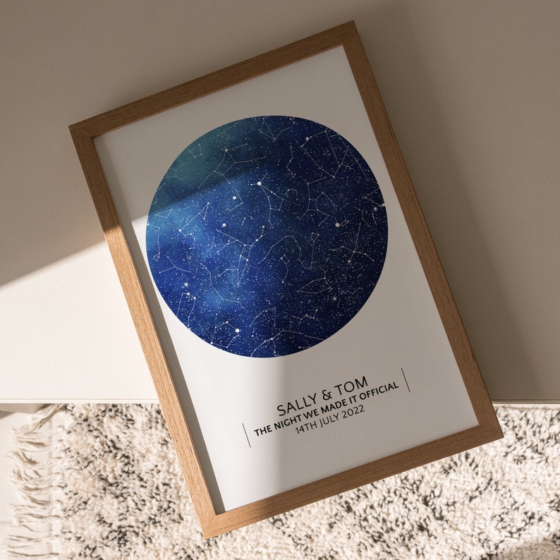 May include: A framed print with a blue watercolor background and white stars. The print features a constellation map with the text "Sally & Tom | The night we made it official | 14th July 2022".