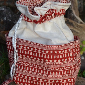 May include: A white drawstring bag with a red and white Christmas tree pattern. The bag has a white drawstring and is made of a soft fabric.