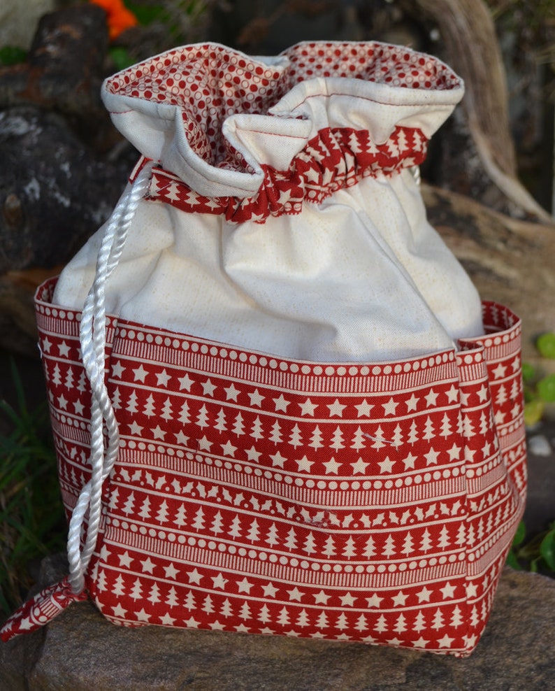 May include: A white drawstring bag with a red and white Christmas tree pattern. The bag has a white drawstring and is made of a soft fabric.