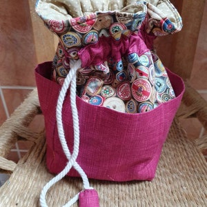 May include: A pink drawstring bag with a white cord and a fabric lining featuring a pattern of colourful vintage spools of thread.