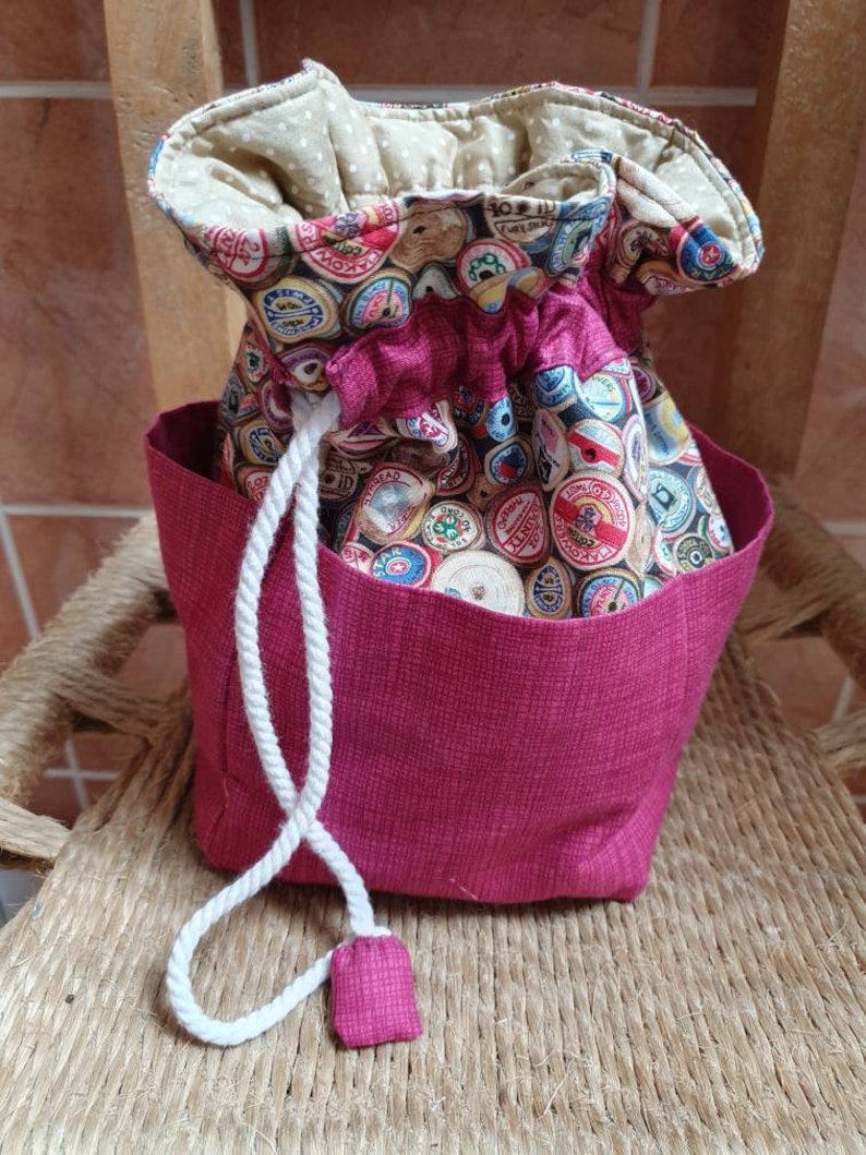 May include: A pink drawstring bag with a white cord and a fabric lining featuring a pattern of colourful vintage spools of thread.