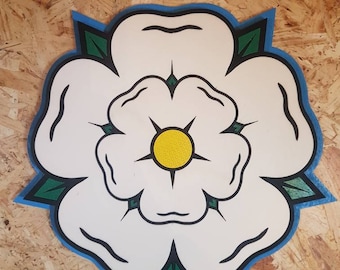 May include: A white flower with a yellow center, surrounded by green leaves, on a blue background. The flower is a stylized representation of the White Rose of York.