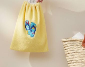 May include: A bright yellow drawstring bag made of soft terry cloth fabric. The bag features an embroidered graphic of a pair of blue flip-flops on the front. It is suspended by a thin blue cord and has a white mesh panel at the top opening.