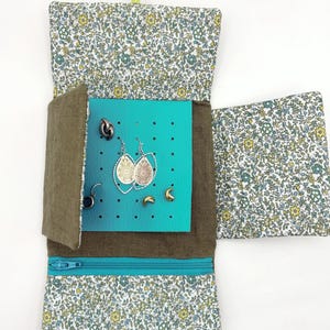 May include: A floral print jewelry organizer with a teal zipper and a teal and blue interior. The organizer is open, displaying several pairs of earrings. The exterior fabric has a white background with small green and yellow flowers.